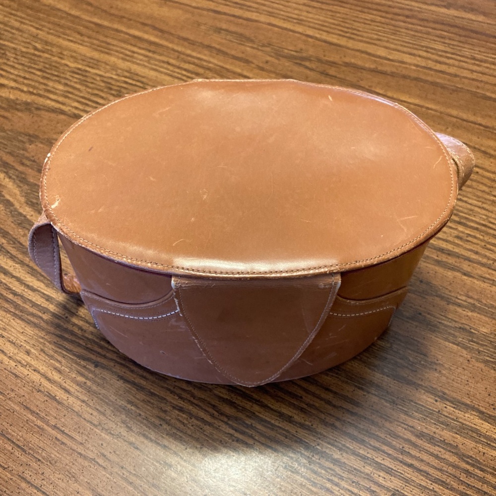 Leather tan oval hand bag. Leather strap. Inside is lined with brown satin.